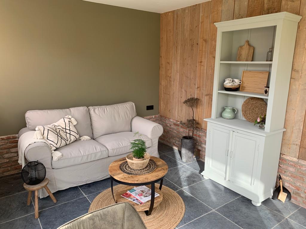 De lichte woonkamer met olijfgroene wand, tweezitsbank en houten vloer